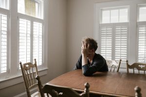 Stressed young man sitting alone at a table in a bright room – Coquitlam mental health therapy and counselling support