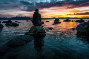 Person sitting on a rock at sunset reflecting by the water – symbolizing body-based healing and somatic therapy in Coquitlam