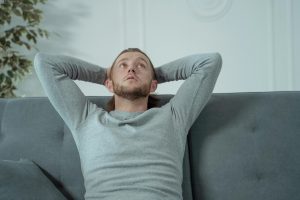 Man lying on couch looking tense while trying to relax, illustrating relaxation-induced anxiety