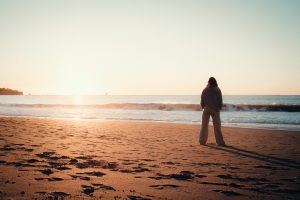 Person standing alone on a beach at sunrise reflecting over feelings of grief. 